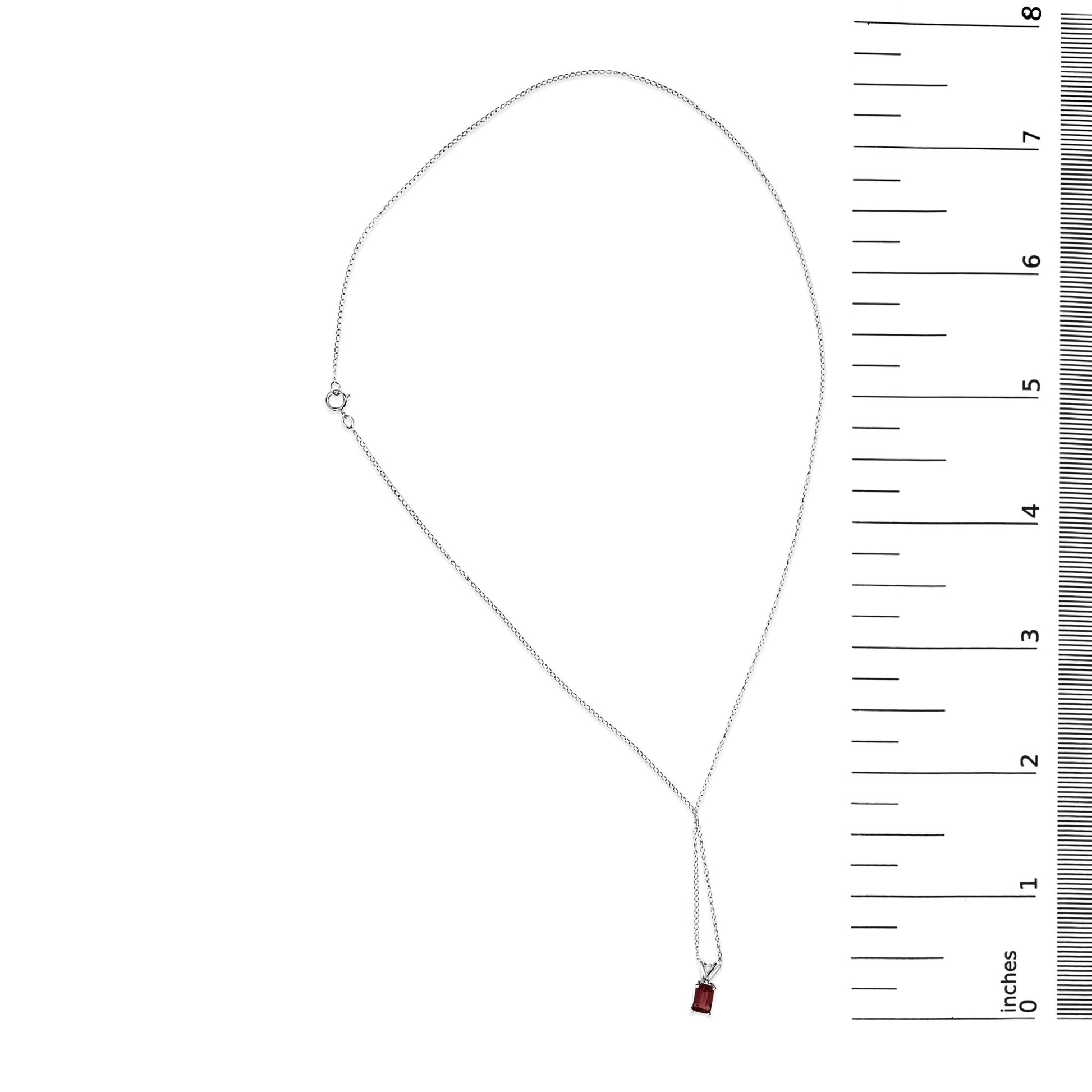 White metal necklace with a single emerald-shaped red gemstone pendant in a 4-prong setting, shown flat on a scale, top-down view.