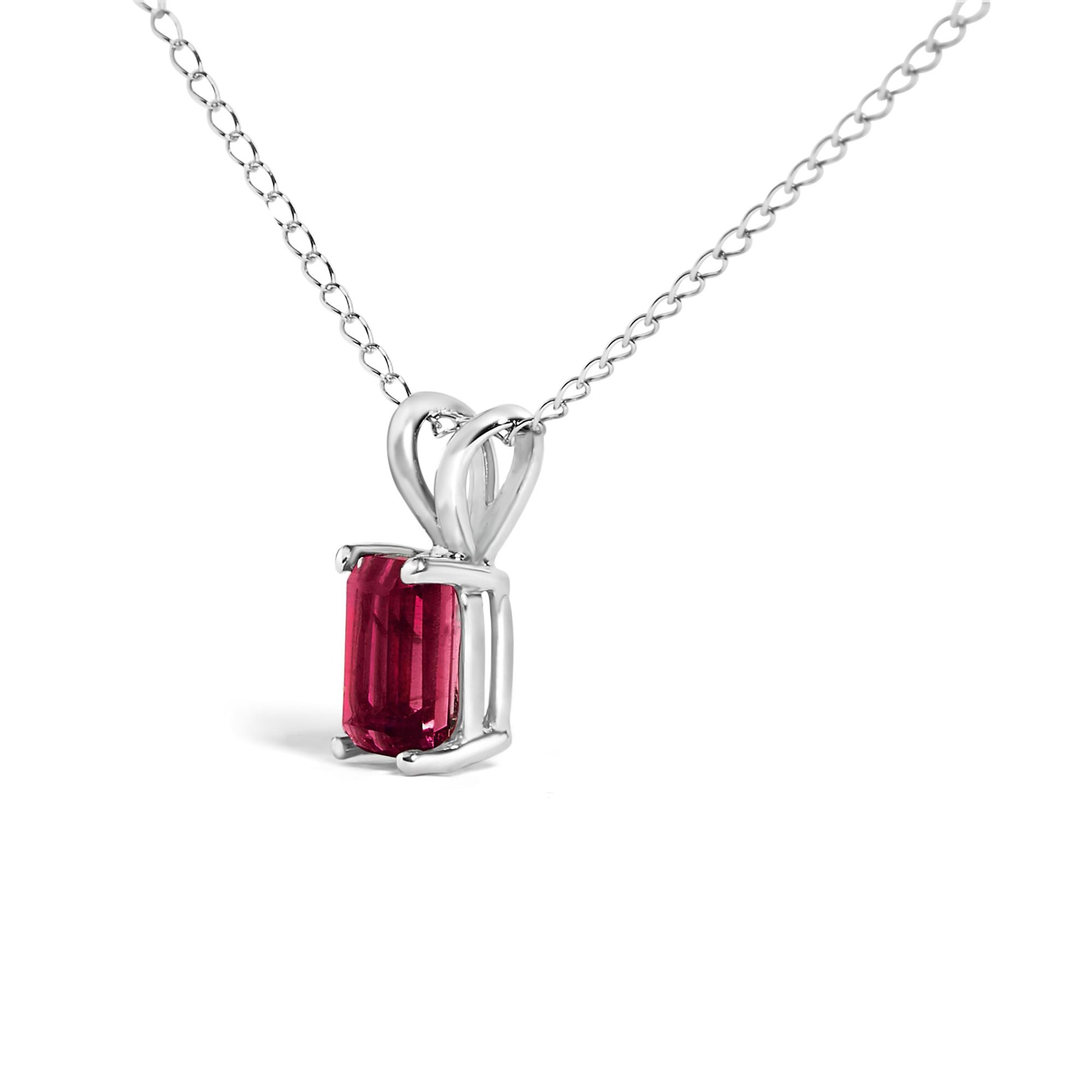 Close-up front angled view of a white metal necklace with a single red emerald-shaped gemstone pendant in a four-prong setting on a chain.