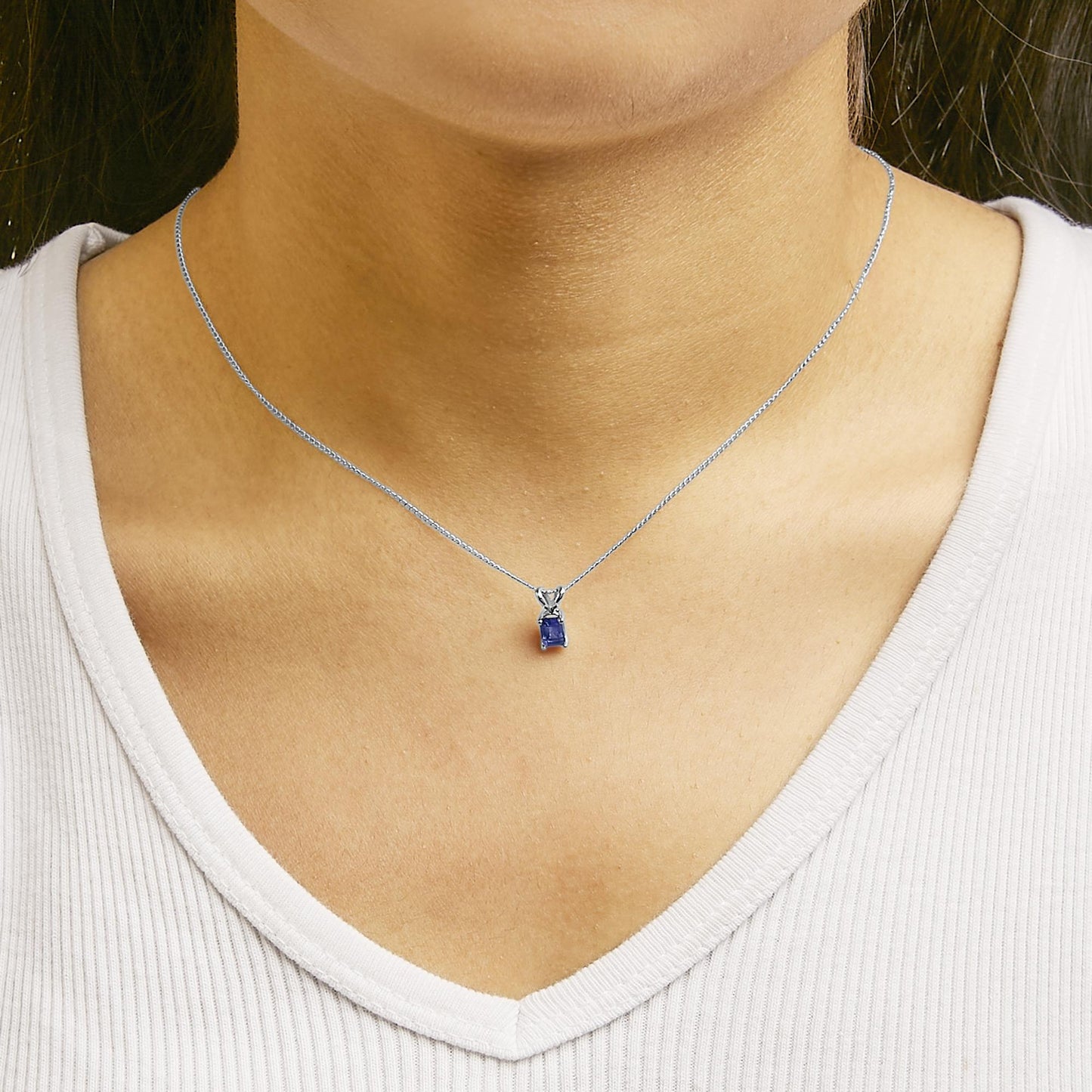 Close-up front angle of a model wearing a white metal necklace with a blue emerald-shaped gemstone pendant in a four-prong setting.