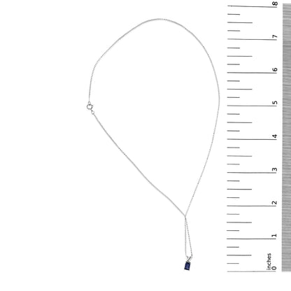 White necklace with a small blue emerald-shaped gemstone pendant set in a 4-prong setting, shown flat on a scale, top-down angle.