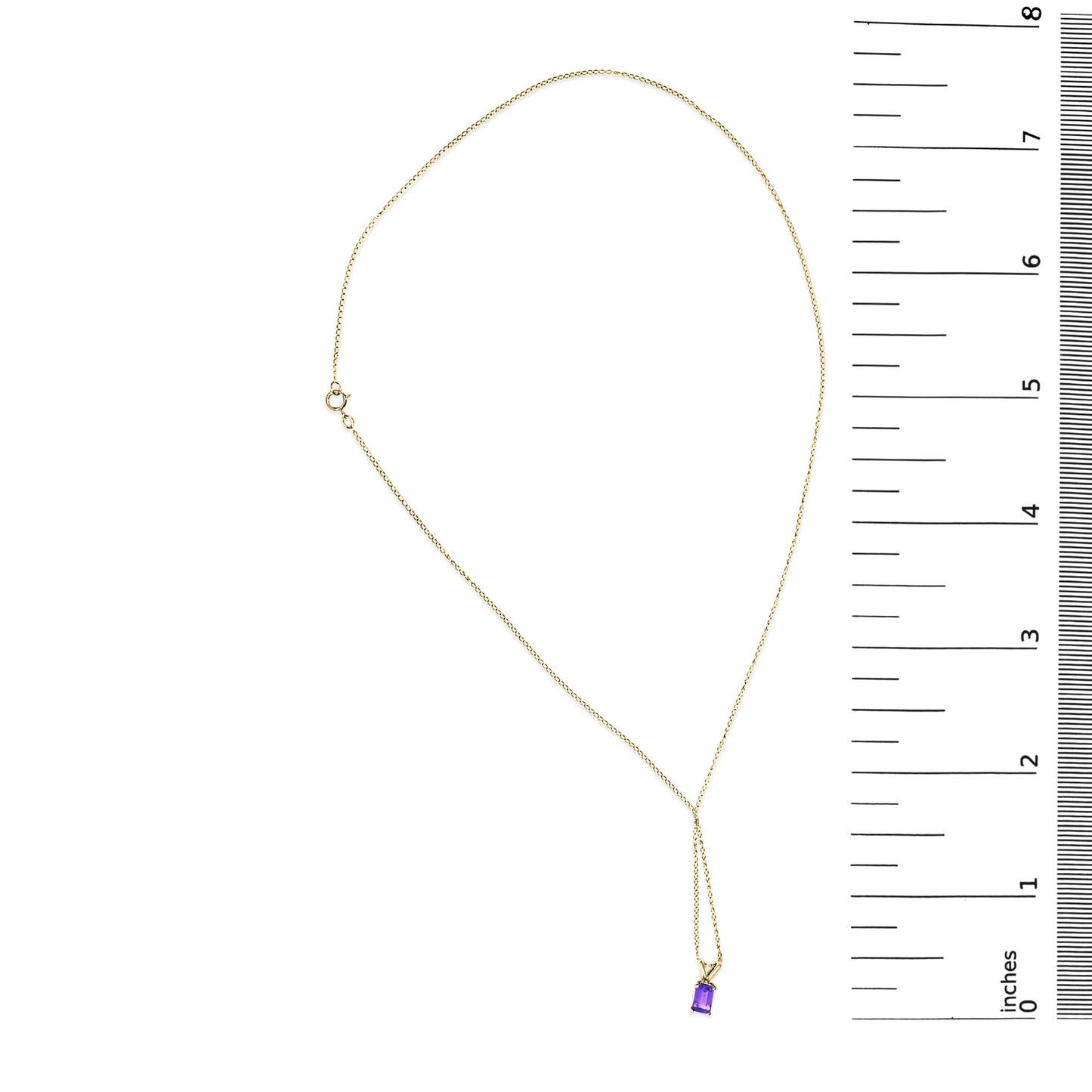 Yellow metal necklace with a small emerald-shaped purple gemstone pendant in a 4-prong setting, shown on a scale. Shot from above.