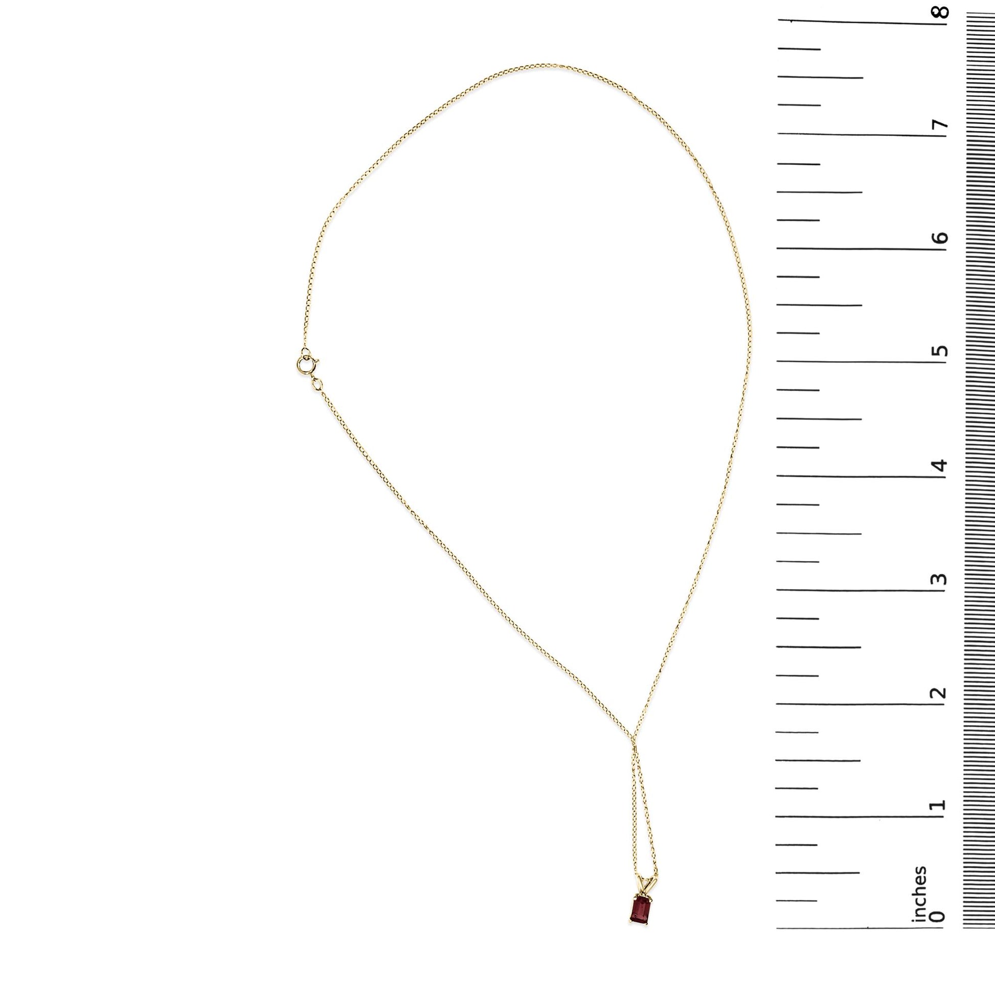Yellow metal necklace with a red emerald-shaped gemstone pendant in a 4-prong setting, shown flat on a scale, top-down angle.