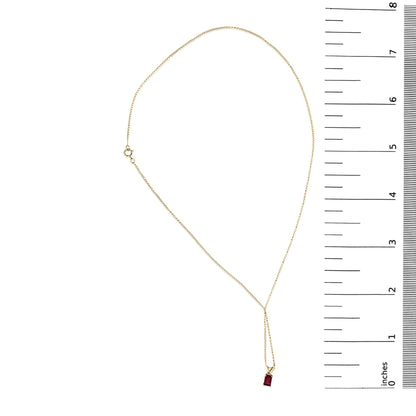 Yellow necklace with a small red rectangular gemstone pendant in a 4-prong setting, shown flat on a white surface next to a ruler for scale, top-down view.