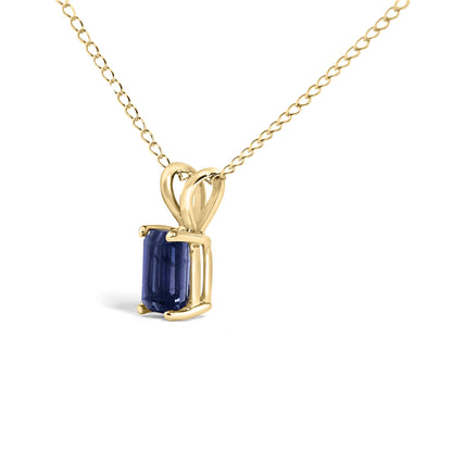 Close-up front angle of a yellow metal necklace with an emerald-cut blue gemstone pendant set in a four-prong setting.