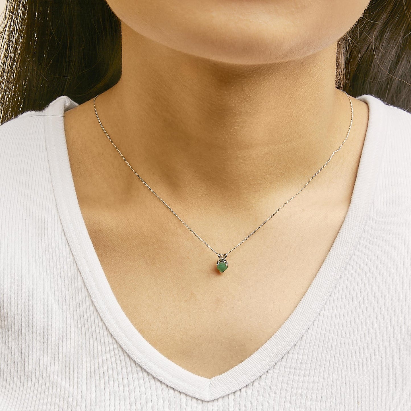 Necklace with a white metal chain and a heart-shaped green gemstone pendant in a 3-prong setting, shown worn on a model from a front angle.