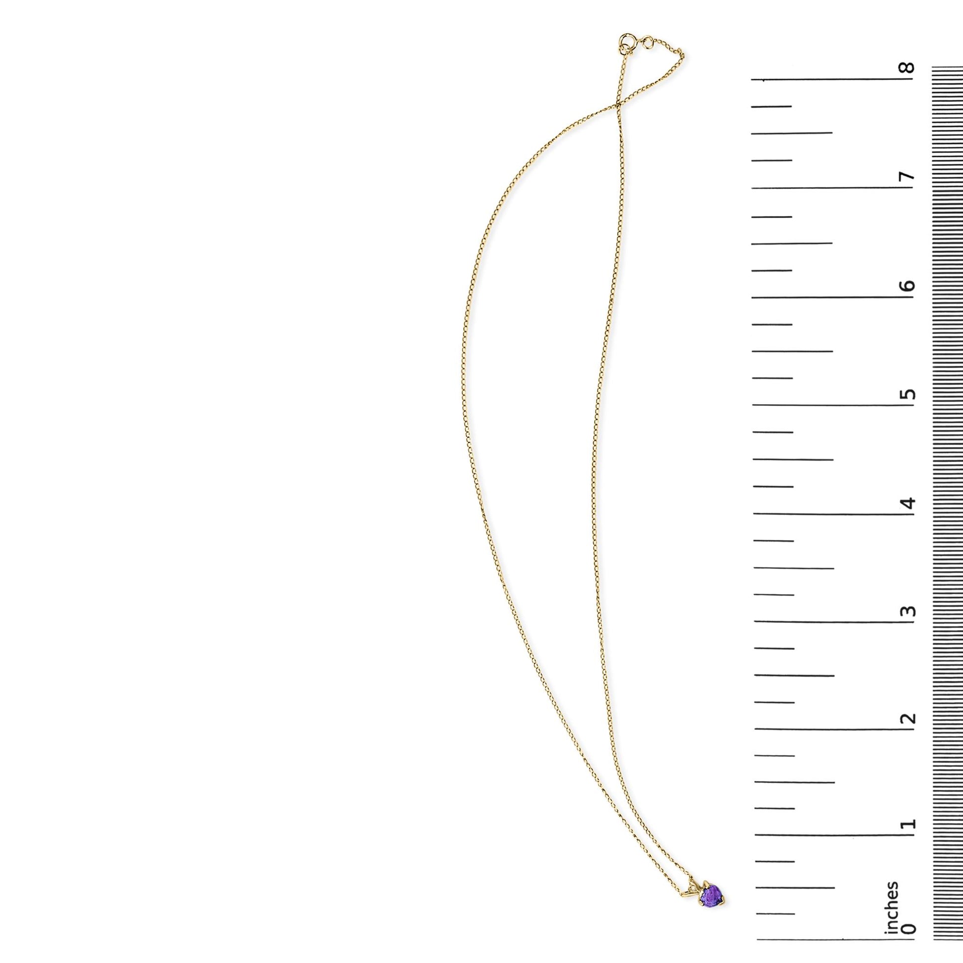Yellow metal necklace with a heart-shaped purple gemstone pendant in a 3-prong setting, shown flat on a white background next to a ruler for scale.