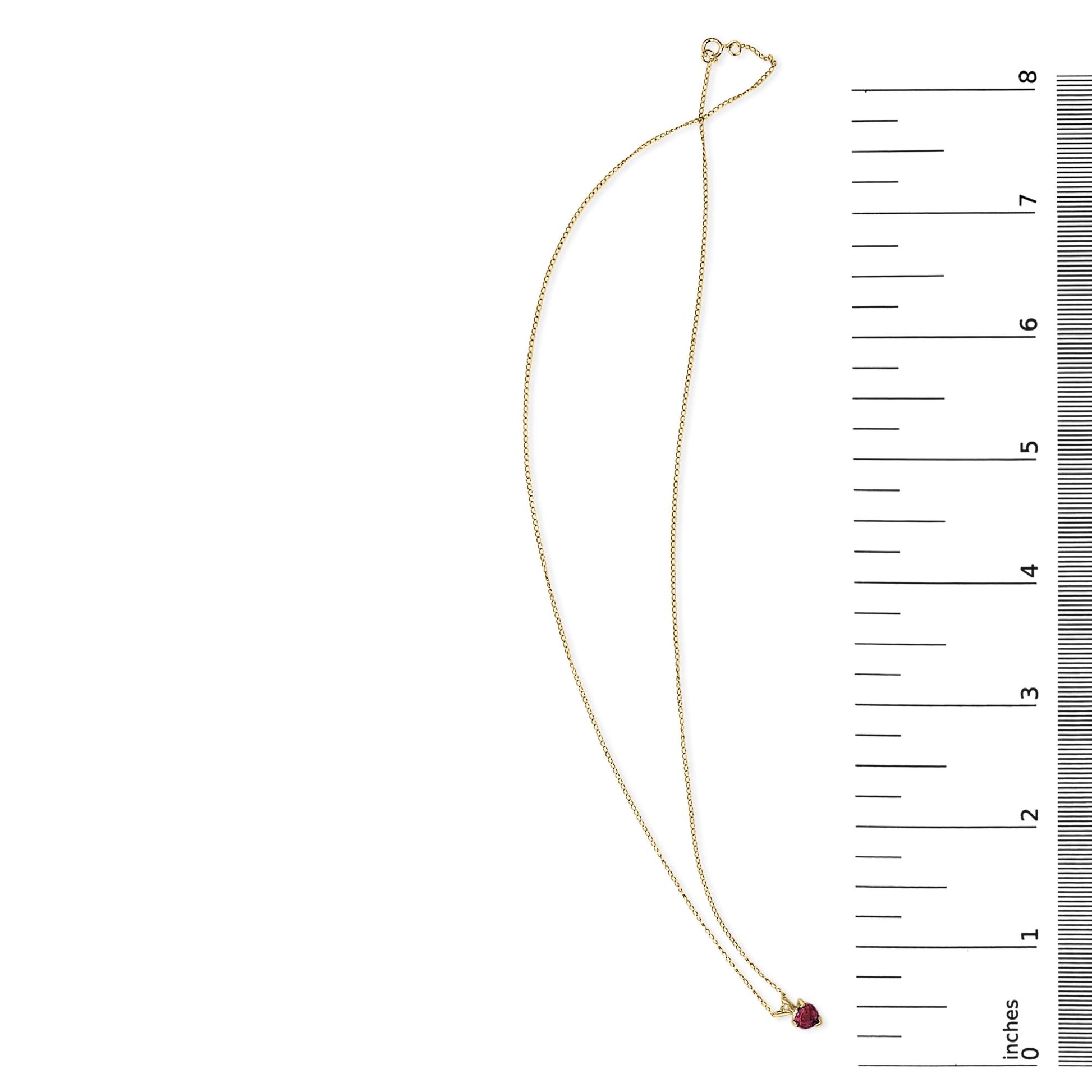Yellow necklace with a heart-shaped red gemstone pendant in a 3-prong setting shown flat on a white surface next to a ruler for scale, top view.
