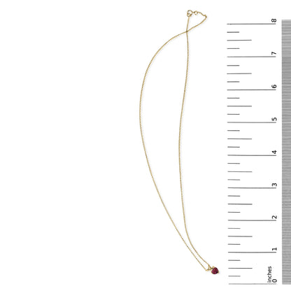 Yellow necklace with a heart-shaped red gemstone pendant in a 3-prong setting shown flat on a white surface next to a ruler for scale, top view.