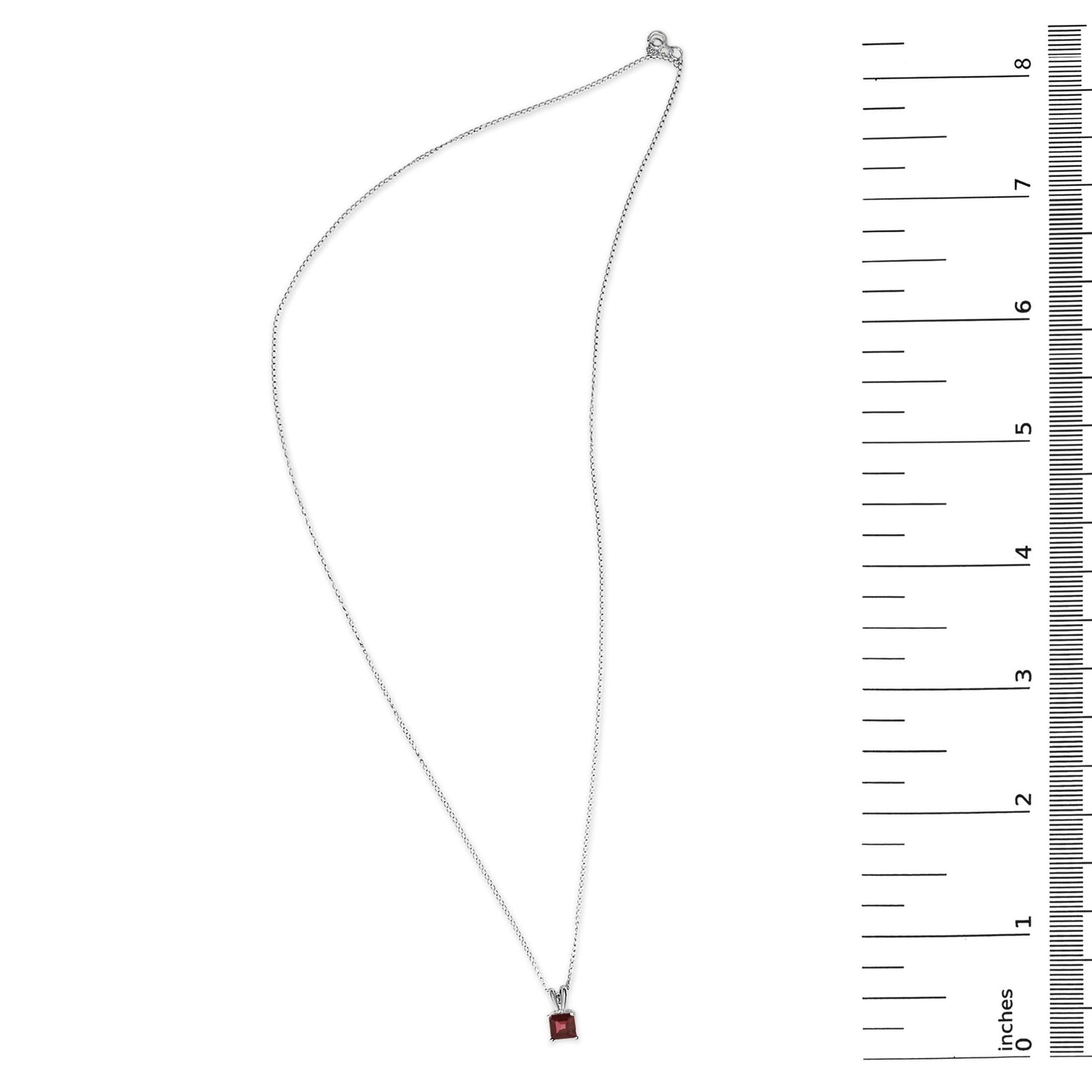 White necklace with a princess-shaped red gemstone pendant in a four-prong setting, shown flat on a surface next to a ruler for scale, top-down angle.