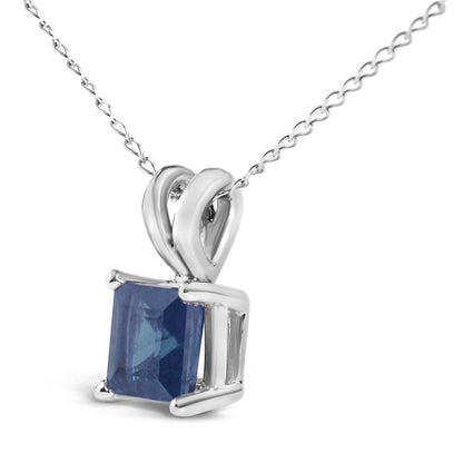 Close-up front angle of a white metal necklace with a pendant featuring a princess-shaped blue gemstone in a four-prong setting.