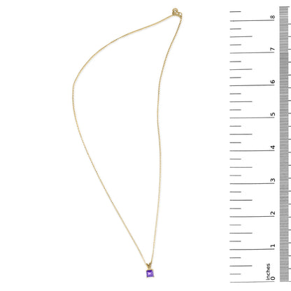 Yellow metal necklace with a square purple gemstone pendant in a four-prong setting, shown on a flat surface with a measuring scale on the right, shot from above.