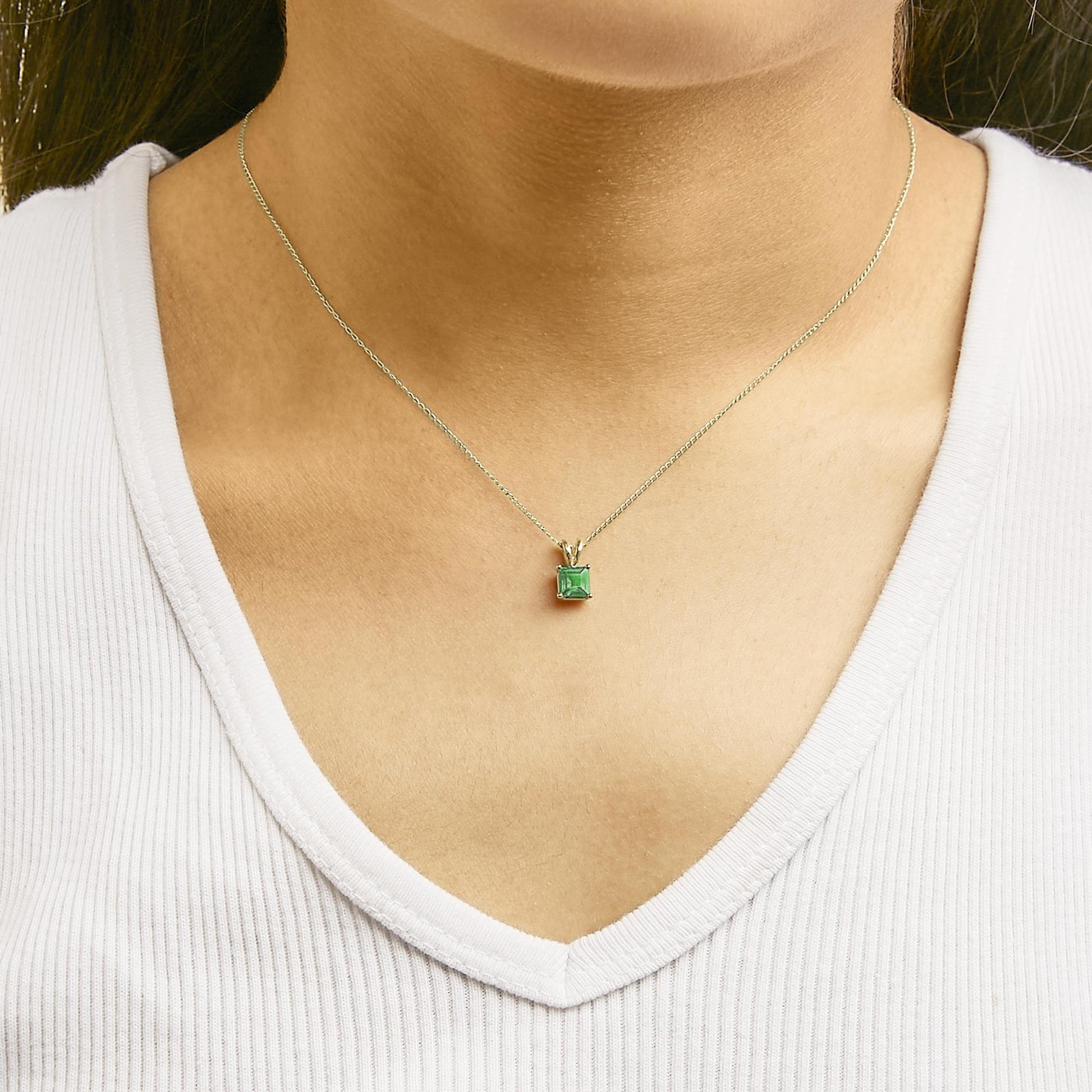 Close-up front view of a model wearing a yellow necklace with a princess-shaped green gemstone pendant in a four-prong setting.