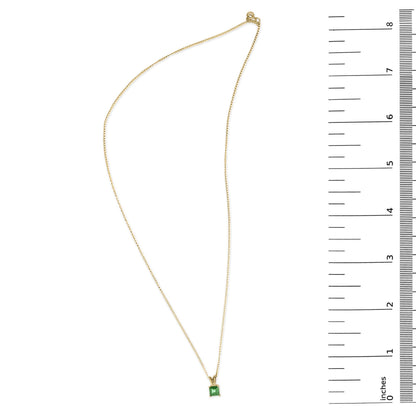 Yellow metal necklace with a green princess-shaped gemstone in a four-prong setting, shown from above on a scale.