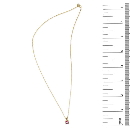 Yellow necklace with a princess-shaped red gemstone pendant in a 4-prong setting, shown on a scale from a top-down angle.