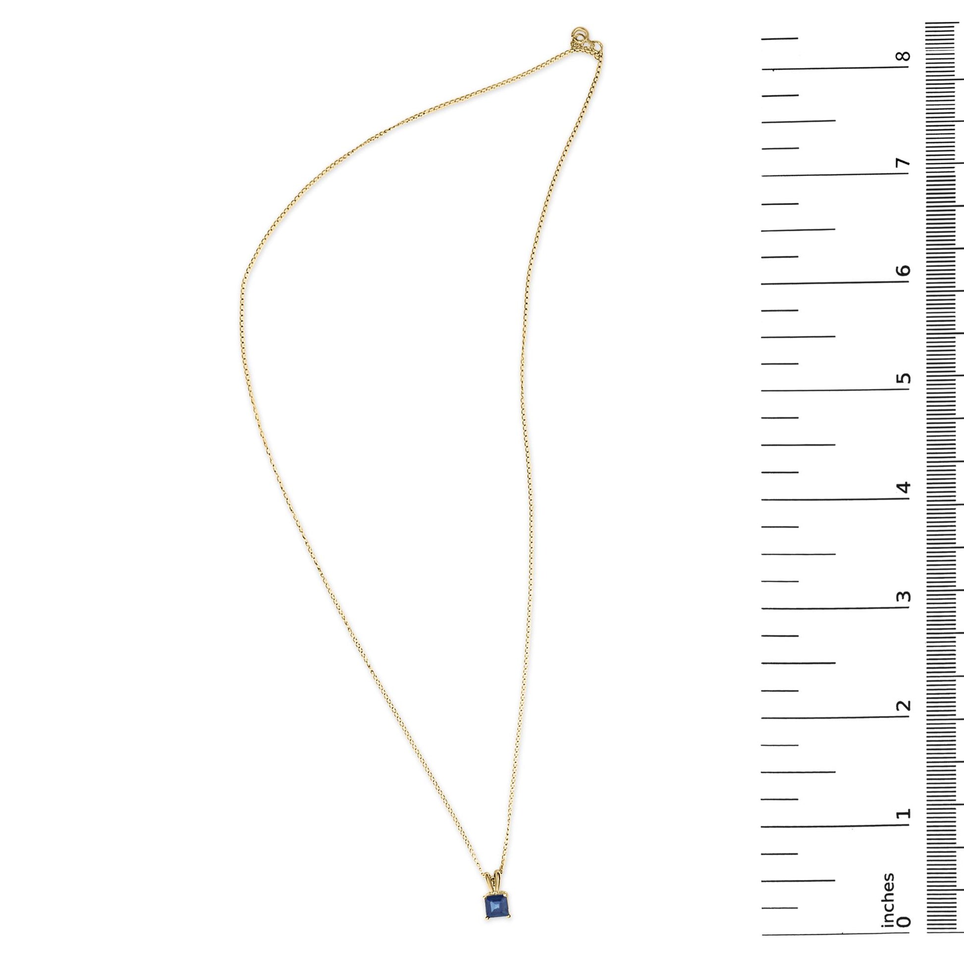 Yellow metal necklace with a princess-shaped blue gemstone pendant in a 4-prong setting, shown flat on a scale from above.