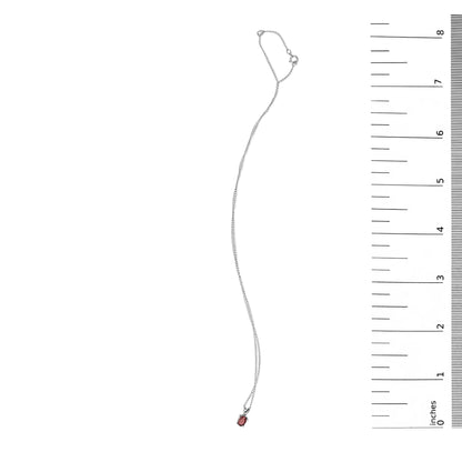 White necklace with a thin chain and an oval red gemstone pendant in a four-prong setting, shown flat next to a ruler scale, top-down view.
