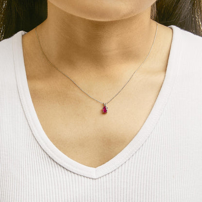 Necklace with a white metal chain featuring a small oval red gemstone pendant in a four-prong setting, shown worn on a model from the front angle.