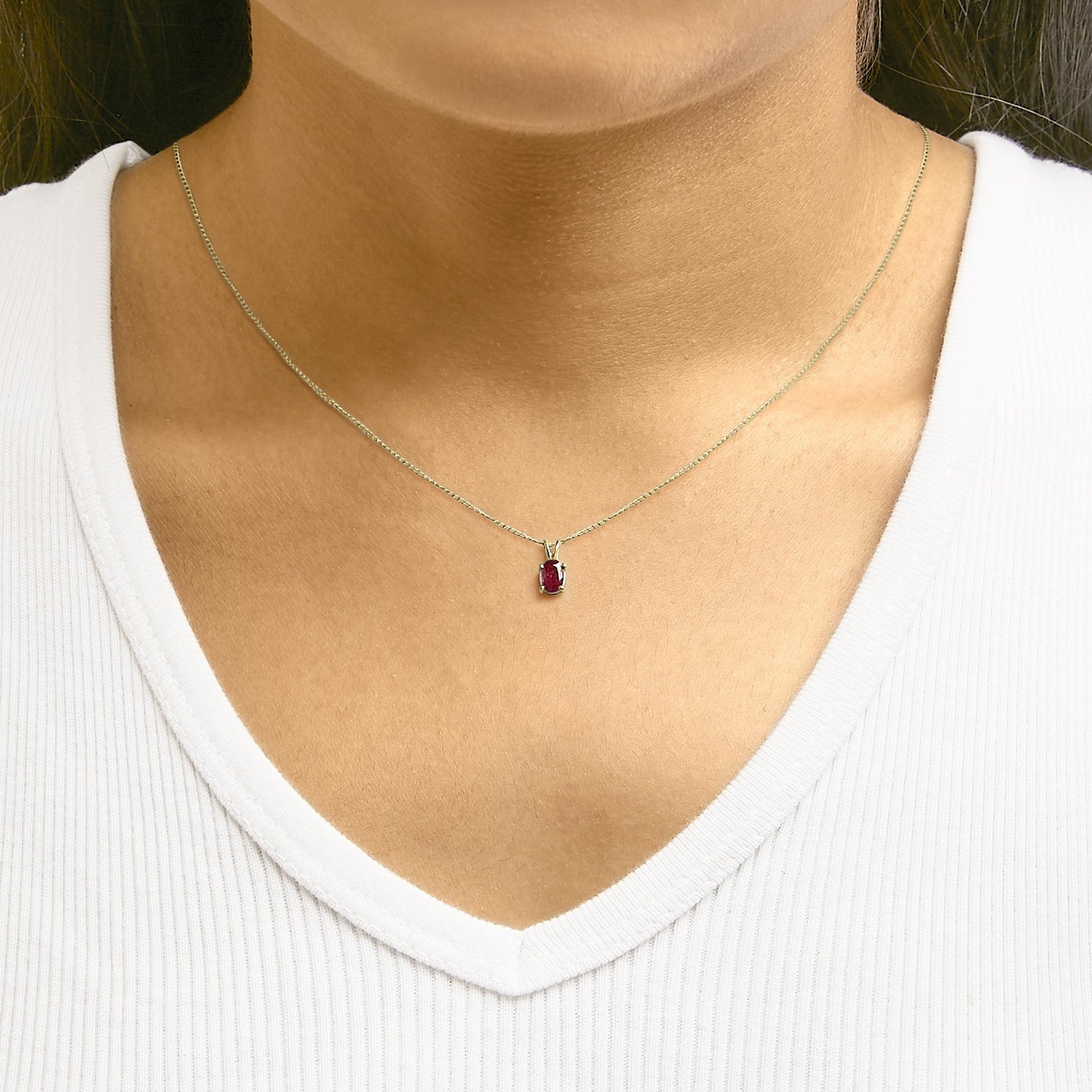Close-up front view of a model wearing a yellow necklace with an oval-shaped red gemstone pendant in a four-prong setting.