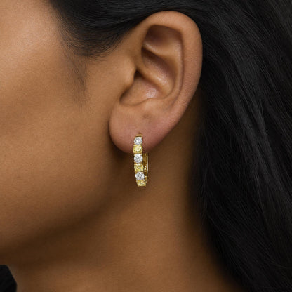 Close-up side view of a model wearing hoop earrings with alternating yellow cushion-shaped and white round prong-set gemstones on yellow and white metal.