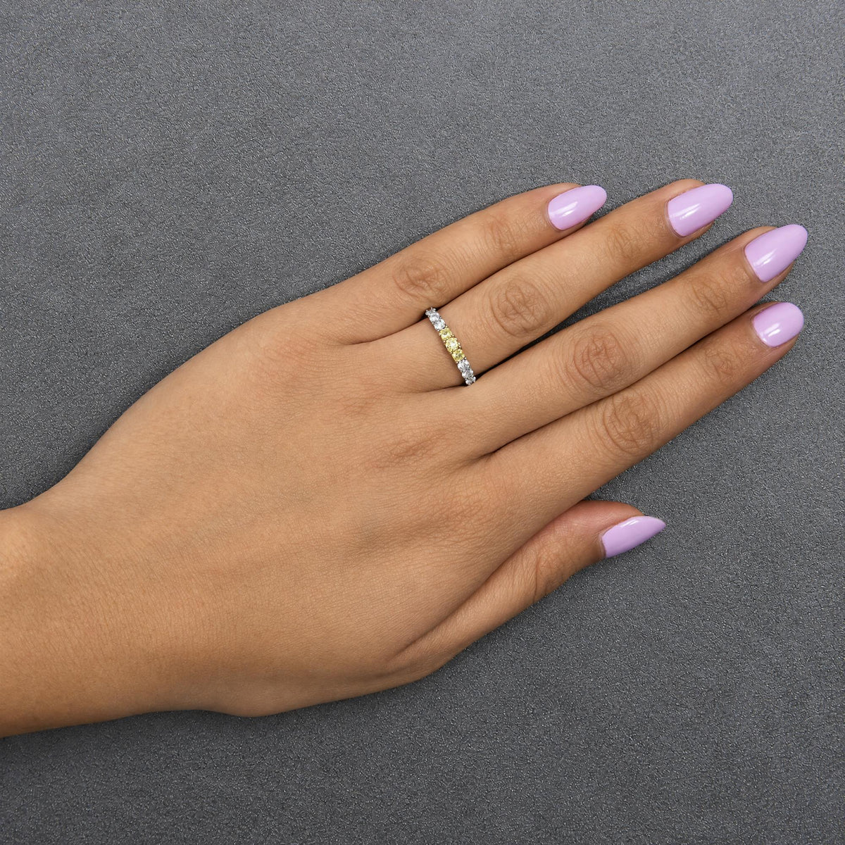 Ring with alternating yellow and white gemstones in prong settings on a band, shown worn on a model's hand in a top-down angle.