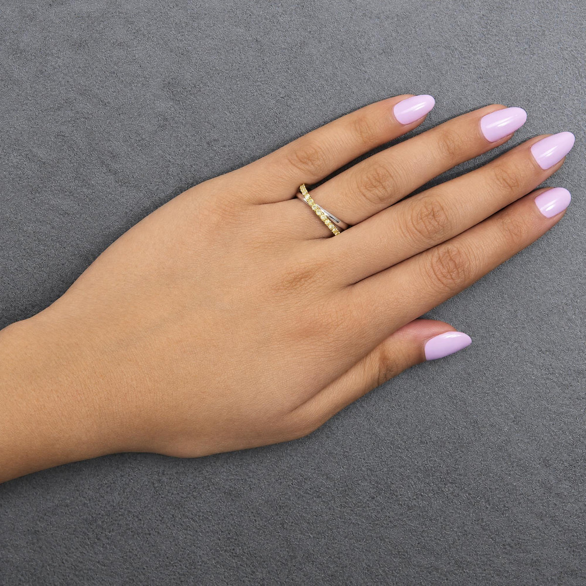 Close-up top view of a hand wearing two rings on the ring finger: one band ring in white metal and one band ring in yellow metal with round yellow gemstones in prong settings.