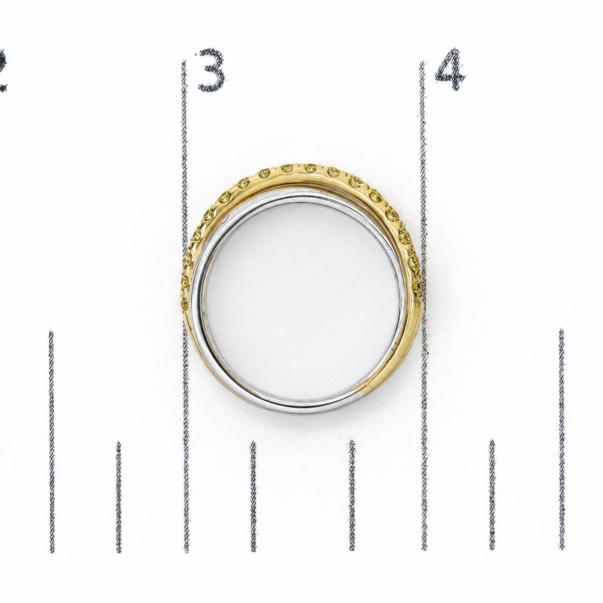 Top-down close-up image of a ring shown on a scale, featuring a two-tone band with yellow and white metal colors, with round yellow gemstones in prong settings all around the yellow metal outer edge.