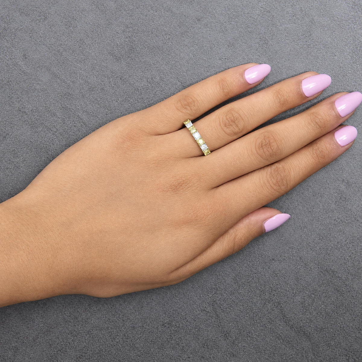 Ring with alternating yellow and white cushion-shaped gemstones in prong settings on a yellow and white band, shown worn on a model's hand, angled top-down view.