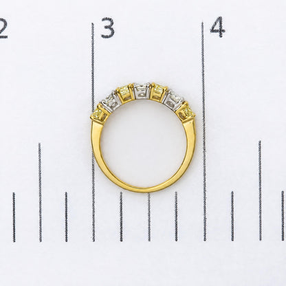 Top-down close-up image of a yellow and white metal ring with alternating yellow and white cushion-shaped gemstones in prong settings, shown on a measurement scale.