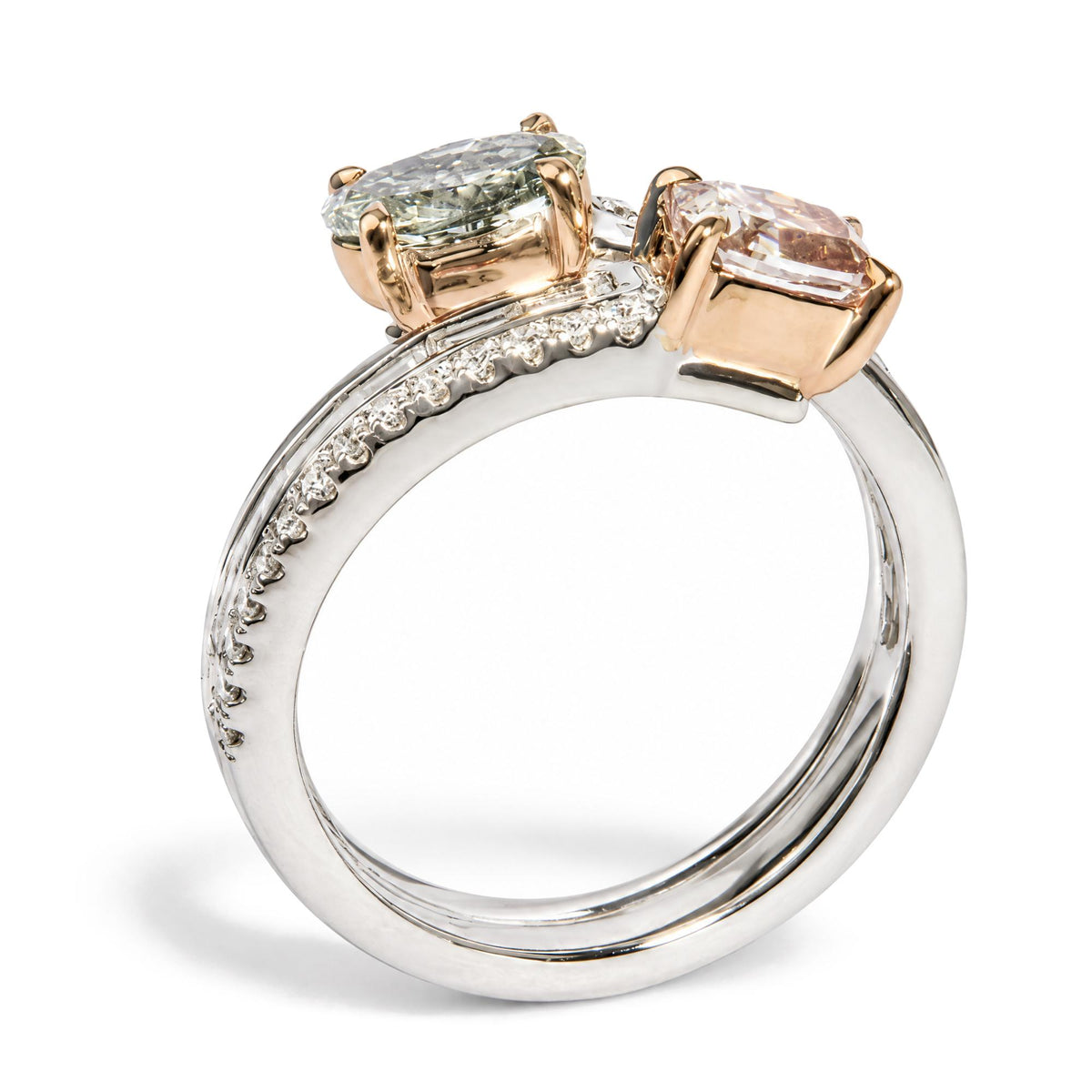Close-up angled view of a white and rose metal ring featuring a cushion-shaped pink gemstone and an oval-shaped green gemstone set in prongs, with multiple round white gemstones in prong settings along the band and white baguette-shaped gemstones in channel settings.