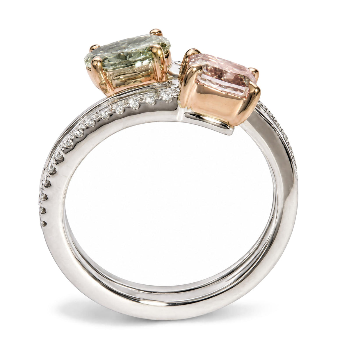 Close-up side angle of a white and rose metal ring featuring two prong-set cushion pink and oval green gemstones, with channel-set baguette white gemstones and prong-set round white gemstones along the white band.