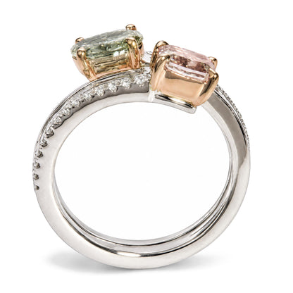 Close-up side angle of a white and rose metal ring featuring two prong-set cushion pink and oval green gemstones, with channel-set baguette white gemstones and prong-set round white gemstones along the white band.