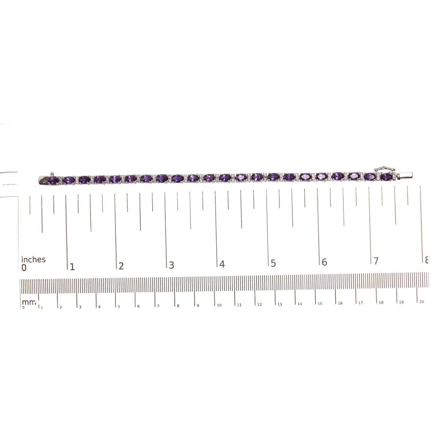 Top-down view of a white metal bracelet with oval-shaped purple gemstones in four-prong settings alternating with round white gemstones in shared prong settings, placed on a ruler for size reference.