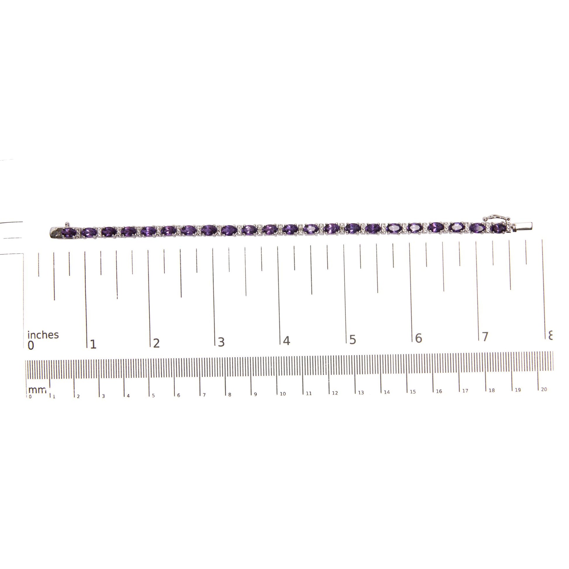 Top-down view of a white metal bracelet with oval-shaped purple gemstones in four-prong settings alternating with round white gemstones in shared prong settings, placed on a ruler for size reference.