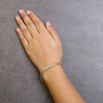 Yellow metal bracelet with round white gemstones in pave setting, shown on a model’s wrist from top angle.