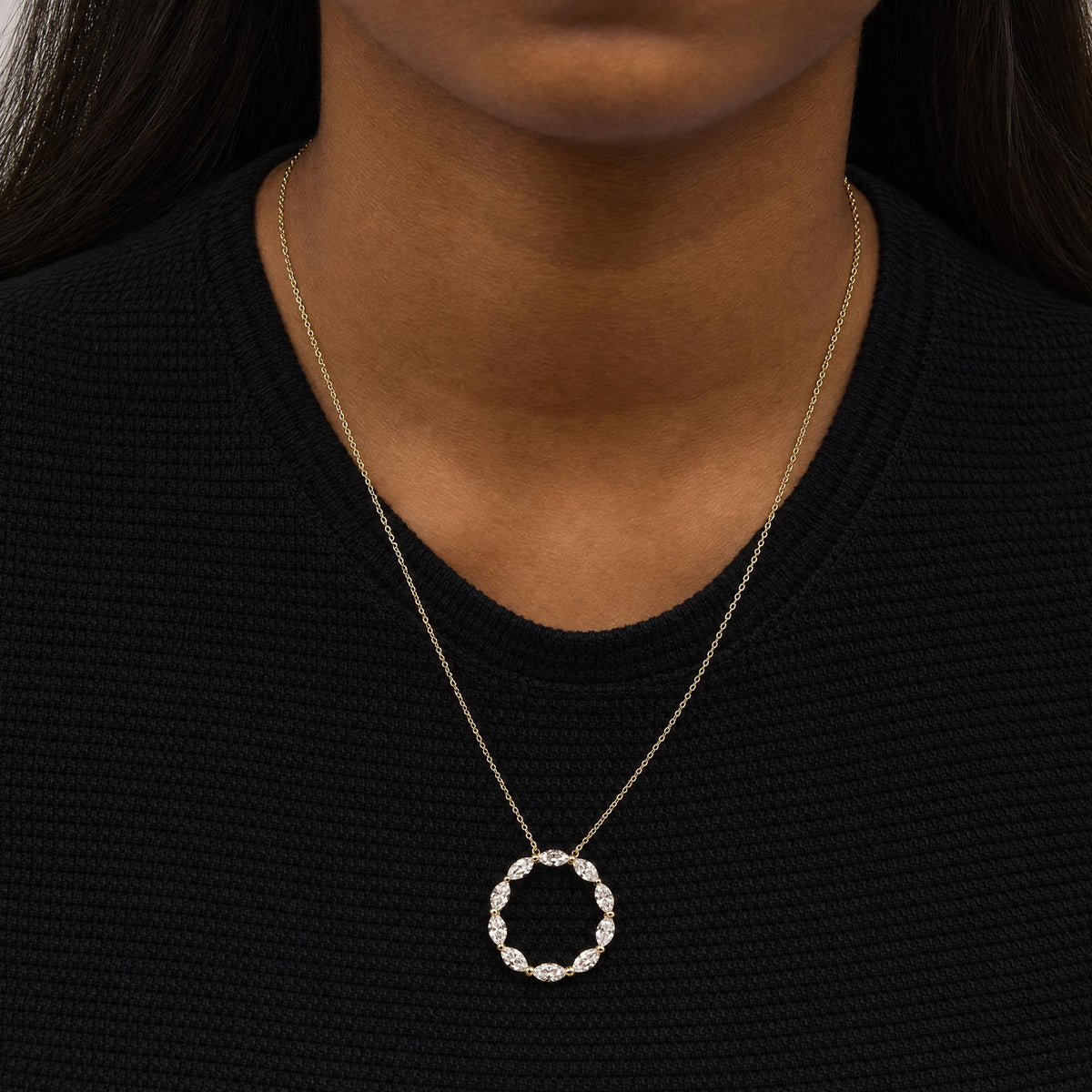 Close-up front view of a model wearing a yellow metal necklace with a circular pendant made of marquise-shaped white gemstones in a shared prong setting.