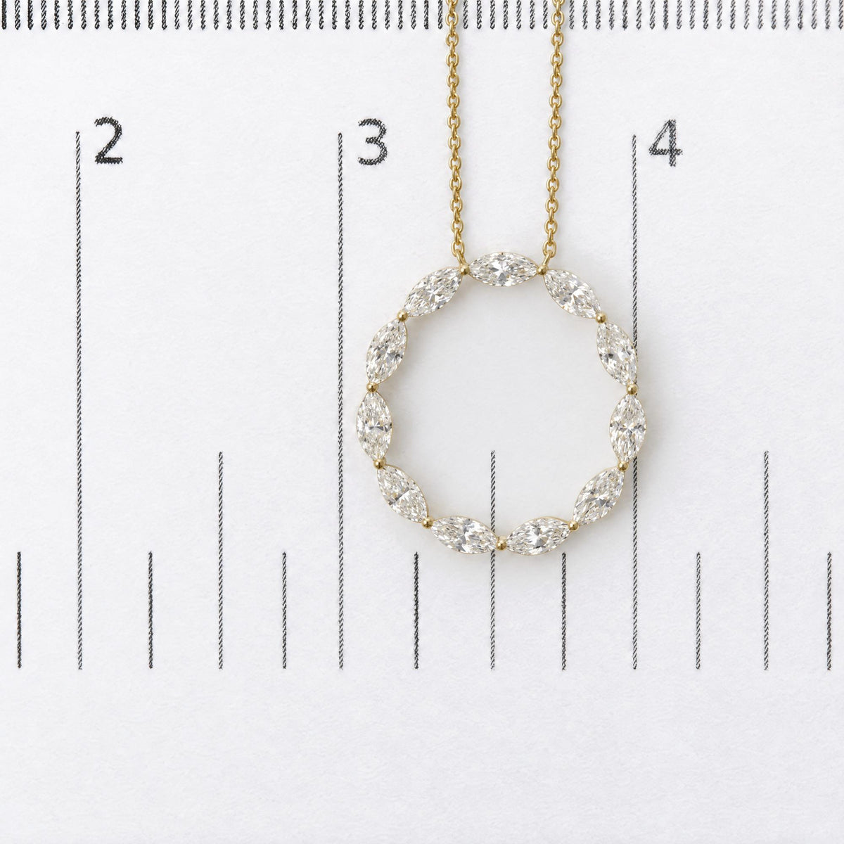 Close-up front view of a yellow metal necklace with an oval-shaped pendant made of marquise-shaped white gemstones in a shared prong setting, shown on a scale.