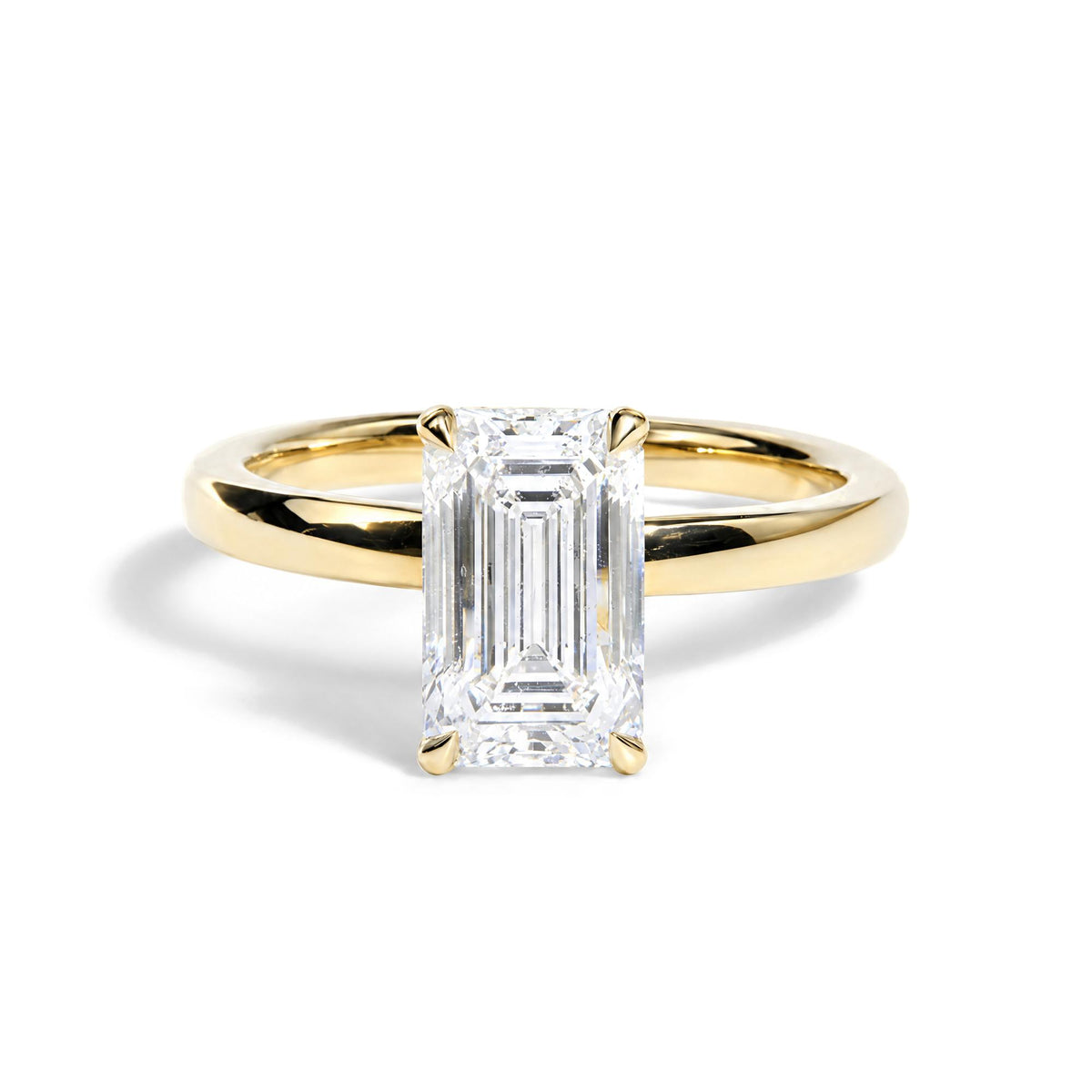 Close-up front angle of a yellow metal ring with a large emerald-shaped white gemstone in a prong setting.