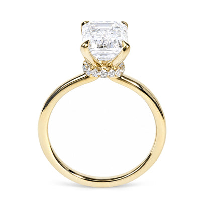 Close-up front view of a yellow metal ring featuring one large emerald-shaped white gemstone in prong setting, surrounded by smaller round white gemstones in prong settings.