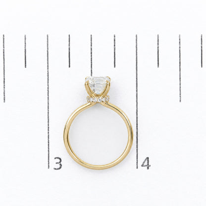 Top view of a yellow-colored ring shown on a scale, featuring a single large emerald-shaped white gemstone in prong setting, surrounded by smaller round white gemstones encircling the base of the main stone.