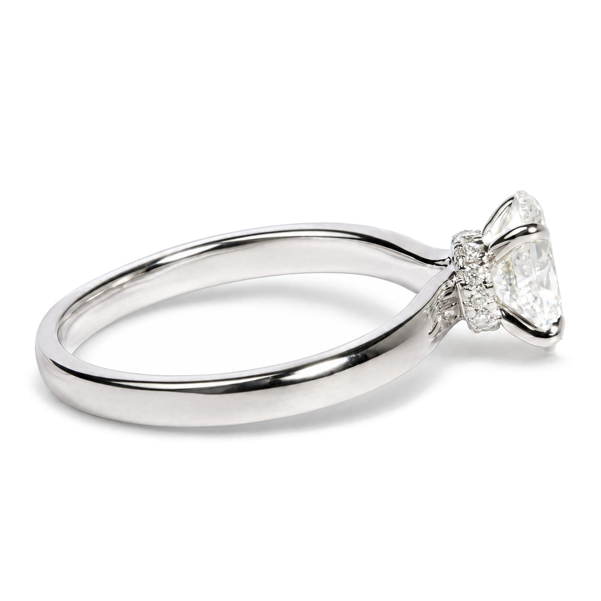 Close-up angled side view of a white metal ring featuring a large oval-shaped white gemstone in a four-prong setting, surrounded by multiple small round white gemstones in prong settings.