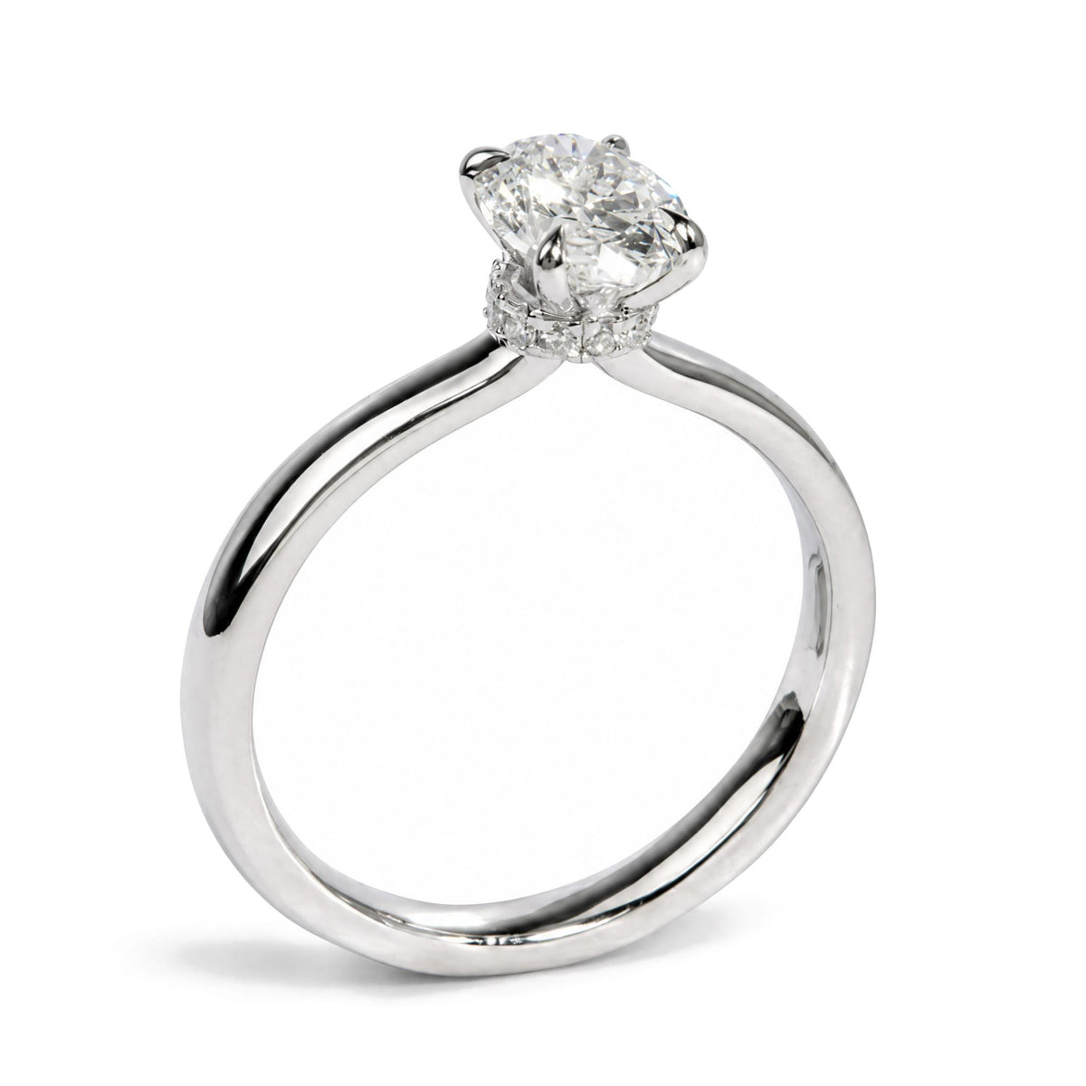 Close-up angled view of a white metal ring featuring an oval-shaped white gemstone in a four-prong setting, surrounded by round white gemstones in prong settings.