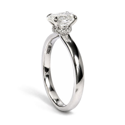 Close-up front angle of a white metal ring featuring one oval-shaped white gemstone held by a four-prong setting, surrounded by multiple round-shaped white gemstones in prong settings along the band.