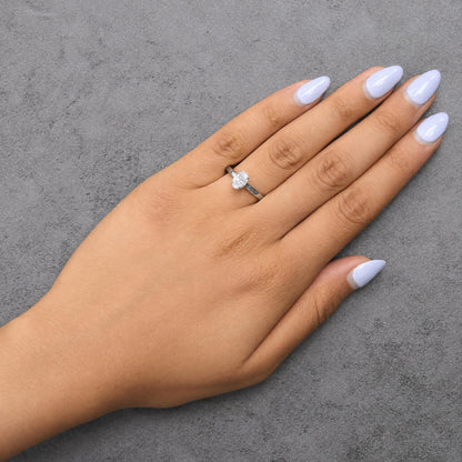 White metal ring with an oval white gemstone in a 4-prong setting and round white gemstones along the band, shown worn on a model's finger, top view angle.