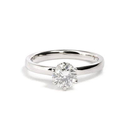 Close-up front angle of a white metal ring featuring a single large round white gemstone in a six-prong setting, surrounded by smaller round white gemstones, shown on a white background.