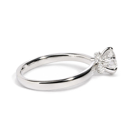 Close-up angled view of a white metal ring with a large round white gemstone in a six-prong setting, surrounded by multiple smaller round white gemstones in prong settings.