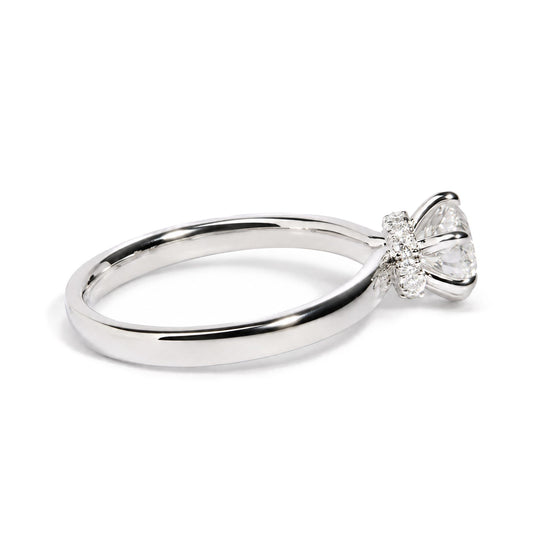 Close-up angled view of a white metal ring with a large round white gemstone in a six-prong setting, surrounded by multiple smaller round white gemstones in prong settings.