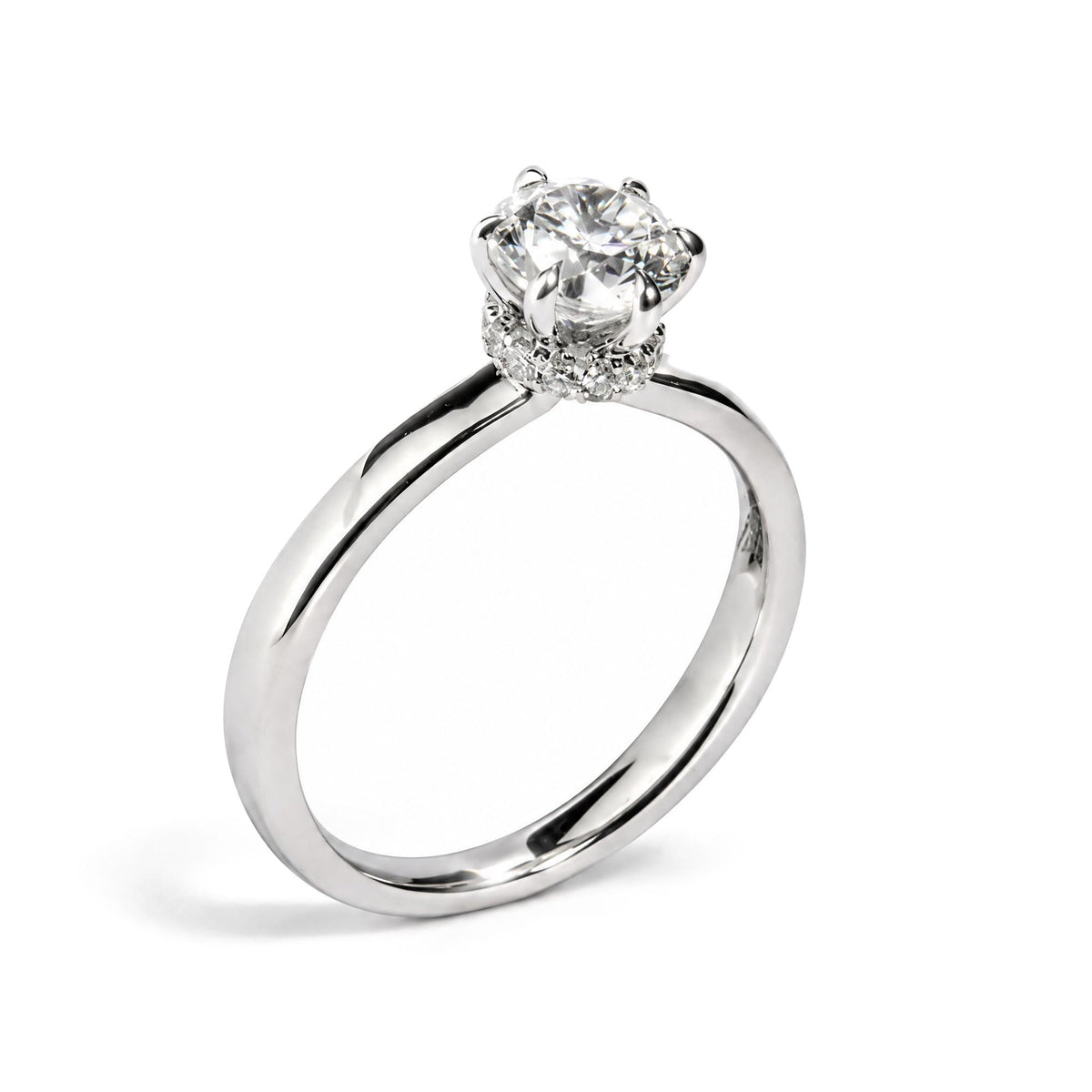 Close-up front angle of a white metal ring with a round white gemstone in a six-prong setting, surrounded by smaller round white gemstones in prong settings on the band.