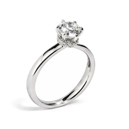 Close-up front angle of a white metal ring with a round white gemstone in a six-prong setting, surrounded by smaller round white gemstones in prong settings on the band.