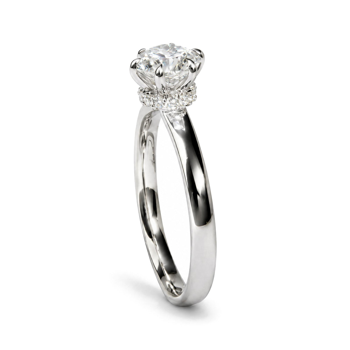 Close-up front angle of a white metal ring featuring a large round white gemstone in a six-prong setting, surrounded by a band of smaller round white gemstones in prong settings.