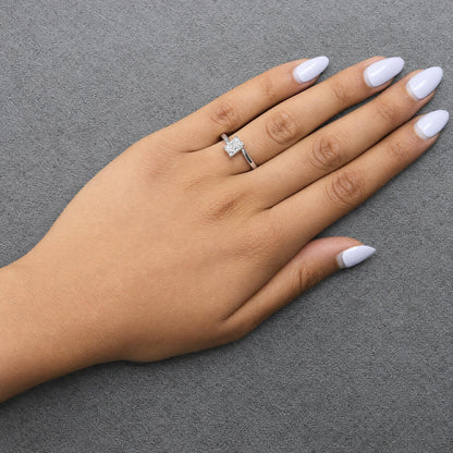 Close-up angled view of a white metal ring with a single radiant shape white gemstone in prong setting, shown worn on a model's finger with light purple nail polish.
